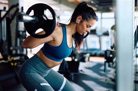 Mujer joven realizando sentadillas en un gimnasio.