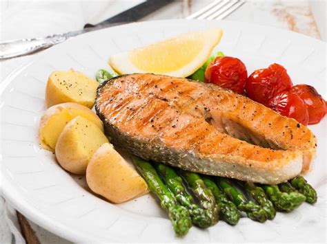 Plato de salmón a la parrilla con hierbas frescas y rodajas de limón, junto a una porción de cantalupo.