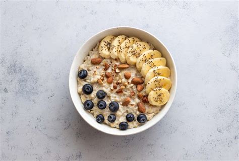 Bol de avena cocida decorado con frutos secos variados, rodajas de plátano y frutos rojos frescos.