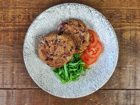 Fotografía de una hamburguesa vegetariana de alubias rojas y arroz servida en pan de hamburguesa con acompañamientos.