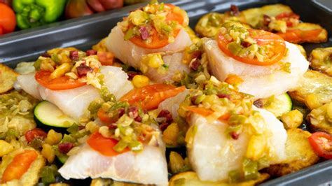 Plato de merluza al horno con verduras variadas y un bol de hummus con crudités