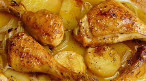 Un pollo asado dorado y jugoso con patatas, cebollas y ajos al horno.
