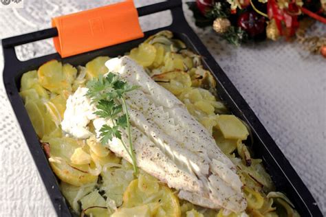Fotografía de una bandeja de horno con pescadilla, patatas, cebolla y zanahorias, horneadas y listas para servir.