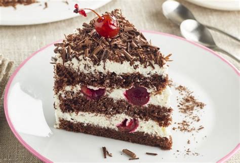 Primer plano de una porción de Tarta Selva Negra mostrando capas de bizcocho de chocolate, nata montada y cerezas.