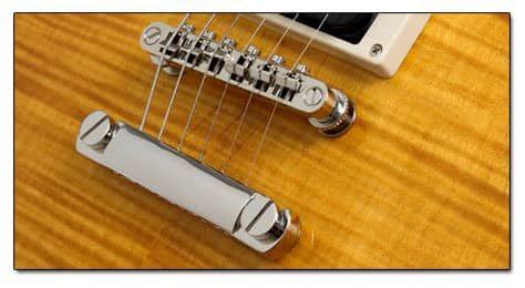 Primer plano de un puente de guitarra con selletas ajustables, ilustrando el mecanismo de ajuste de la altura de las cuerdas.